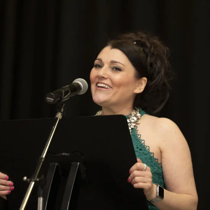 Tracy in action smiling About Tracy Heatley, as Tracy is on stage presenting at a business event.